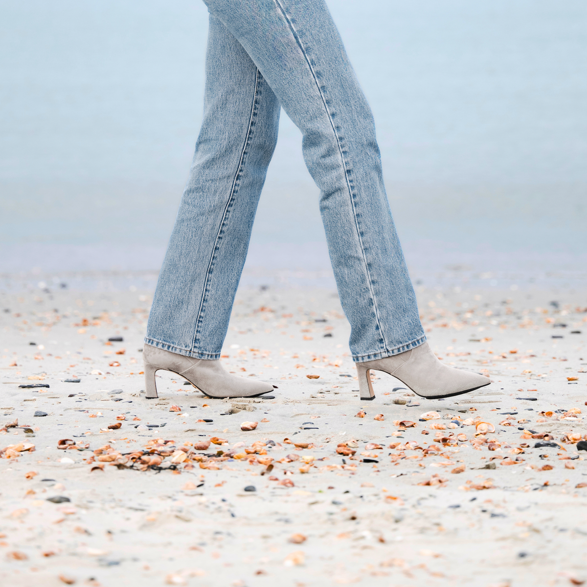Scarlett Chase ankle stretch taupe suede Portia 75 bootie with a block heel | Side view on model walking on beach with jeans