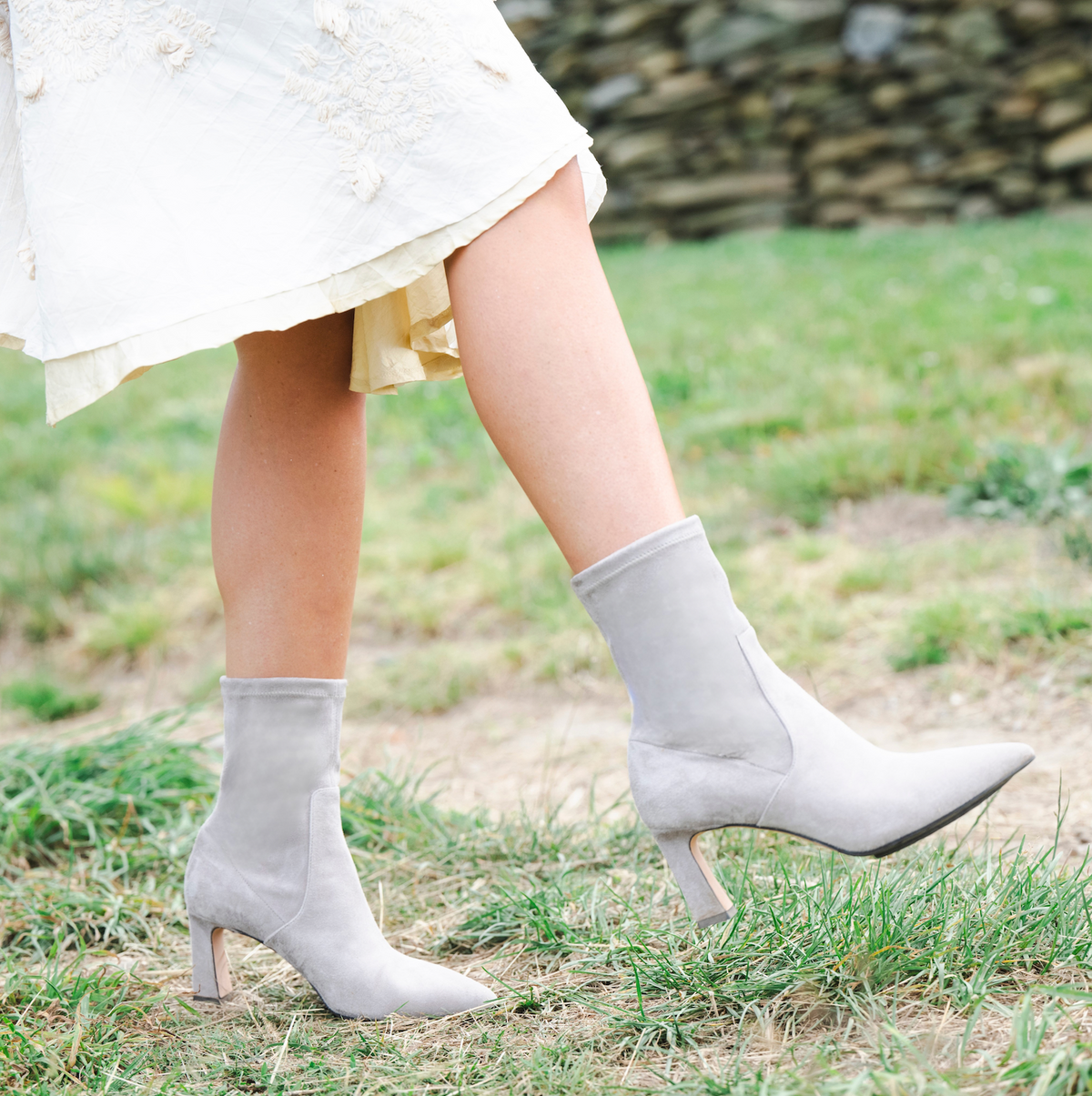 Scarlett Chase ankle stretch taupe suede Portia 75 bootie with a block heel | On model on grass outside walking with front foot off ground and side view of each