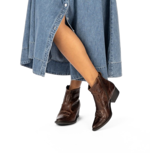 Scarlett Chase Mahogany leather Fiona cowboy bootie with decorative stitching and a side zipper | On feet with long blue dress crossed legs one foot is 3/4 view and off the ground the other is front on view with white background
