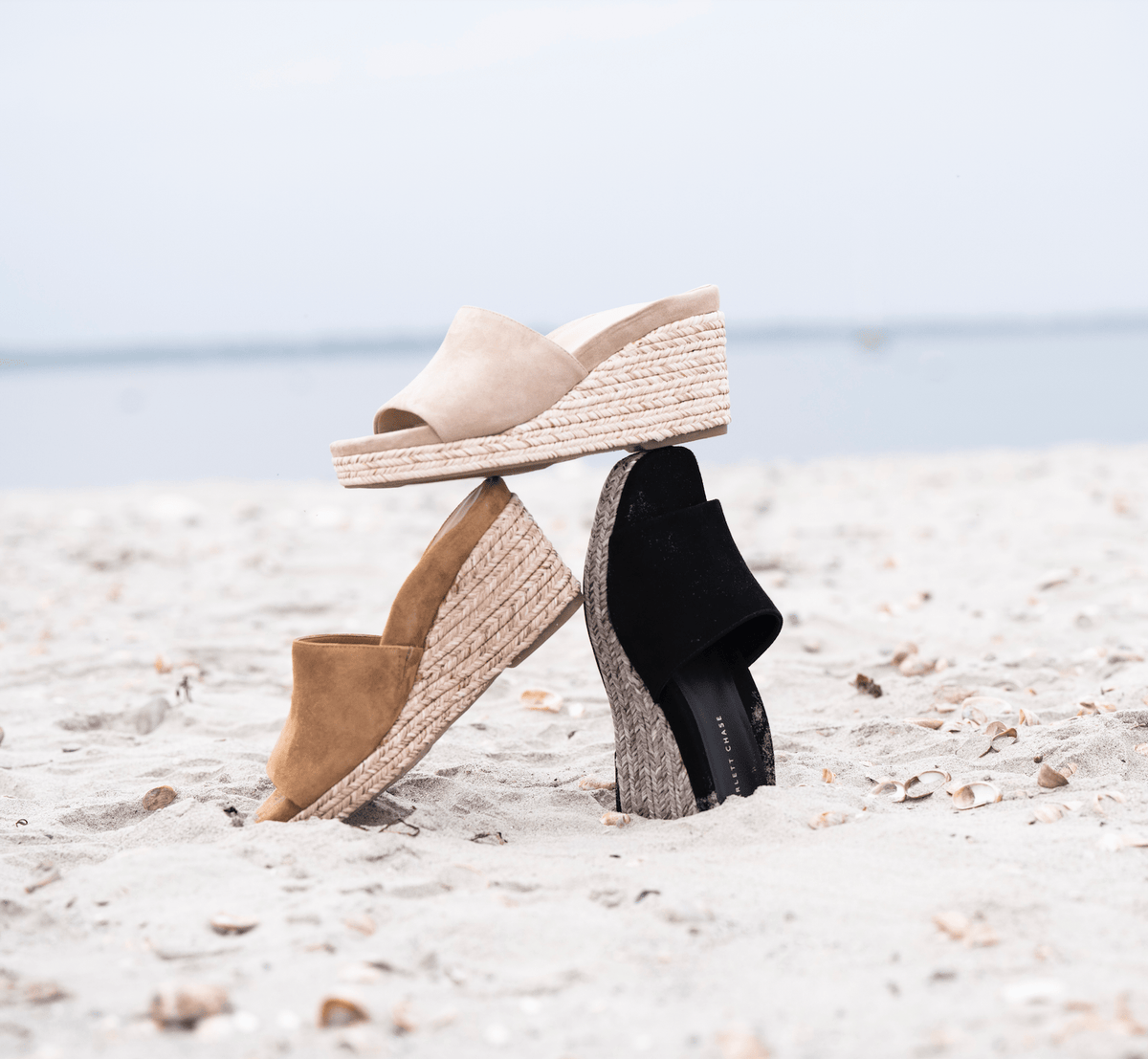 Scarlett Chase Capri Wedge Sandal with a mesh-lined upper and handroped wedge bottom | three single wedge sandals in Sienna, black and sand suede on beach background