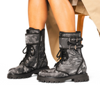Scarlett Chase Athena Combat Boot with a lightweight sole, functioning hardware, and a hidden zipper | | Nylon, Gray camouflage, black piping - person sitting in chair wearing raincoat and bare legs, showing view from the side