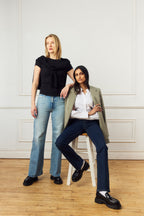 Scarlett Chase Ava Lug Penny Loafer in Black Leather with a lightweight sole and SC coin | Two women posing together (one standing, one sitting) in a room with wooden flooring and white walls.