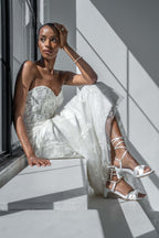 Scarlett Chase Cali 45 white satin dress sandal with wrap-around ties and a gathered front | Woman in a white wedding dress sitting by a window with sunlight casting shadows.