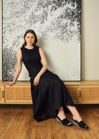 Scarlett Chase Capri Wedge Sandal with a mesh-lined upper and handroped wedge bottom | Woman in black dress/black suede wedge sandals on wooden bench with abstract painting in the background
