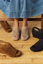 Scarlett Chase Chelsea Wedge Sandal with a perforated leather upper and adjustable back strap | Close-up of feet wearing open-toe sandals on a wooden floor with a skirt and sandals in the foreground (black, sand and Sienna suede).