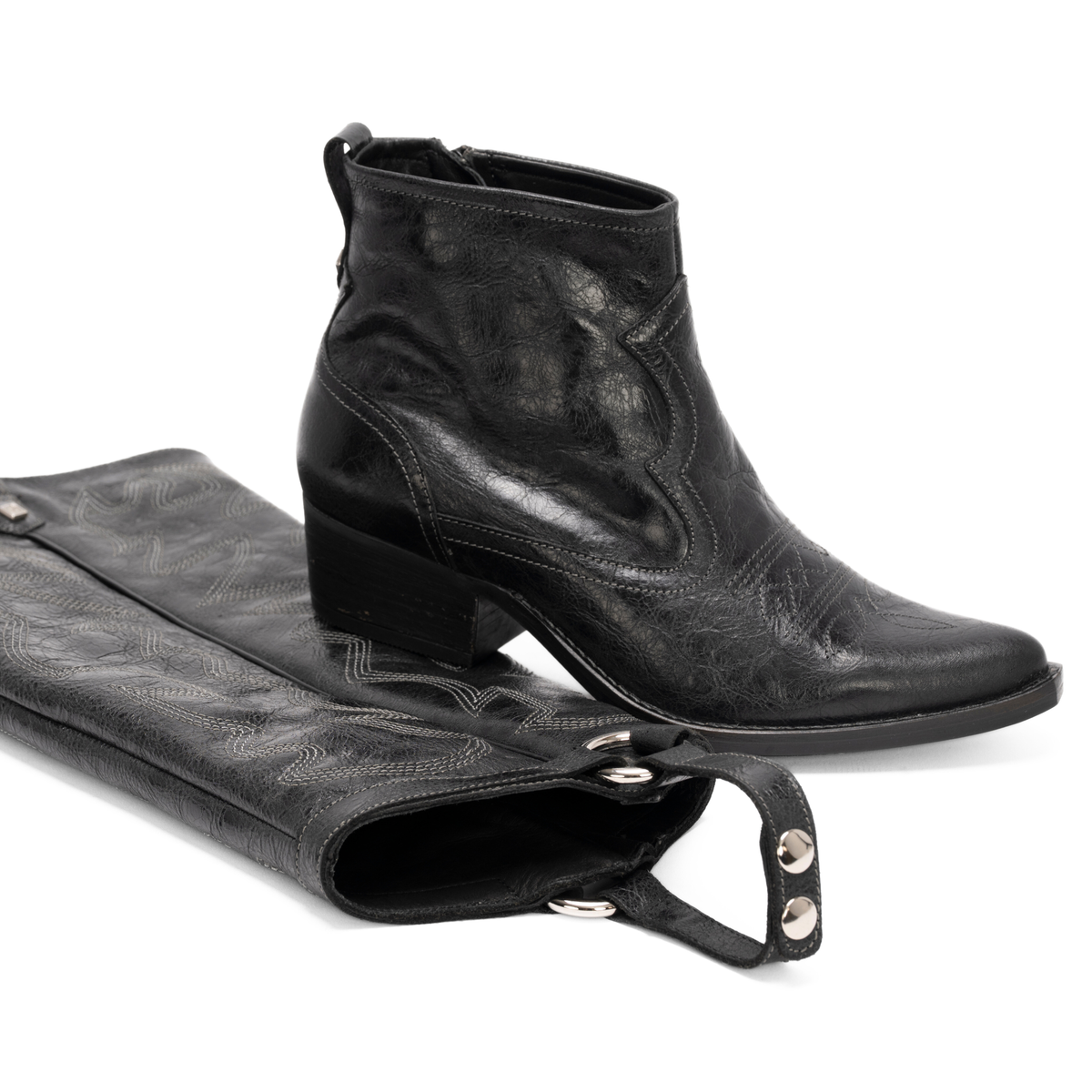 Scarlett Chase black leather Fiona cowboy bootie with decorative stitching and a side zipper and interchangeable knee-high gaiter with decorative sticking and clip-on straps|3/4 view of bootie resting on knee-high gaiter on white background
