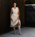 Scarlett Chase knee-high stretch champagne suede Lola 75 boot with a block heel | Model with skirt 3/4 view white flooring and brown background outside