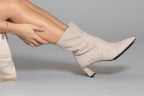 Scarlett Chase ankle stretch champagne suede Maya 55 bootie with a block heel | On model sitting on floor knees bent side view heels on ground toes in air on gray background