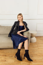 Scarlett Chase ankle stretch black suede Portia 75 bootie with a block heel | 3/4 view on model sitting on tan couch with wooden floor and white background