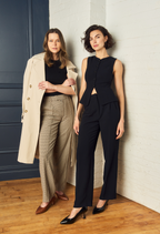 Scarlett Chase Soiree 75 Pump Black Patent with a V-cut upper and sculpted heel and the Amore 55 Pump in Sumatra Croc with a rounded upper and a block heel | Two models standing together in professional wear against a white and blue wall and a wooden floor