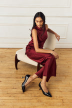 Scarlett Chase Soiree 75 Pump Black Patent with a V-cut upper and sculpted heel | Overhead view of a model sitting on a white chair while sitting with legs crossed on a wood floor