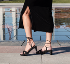 Scarlett Chase noir metallic velvet upper Cali 45 dress sandal with wrap-around ties and a gathered front | On model feet profile view front foot heel lifted back shoe laying flat on stone walkway by waterfront outside 