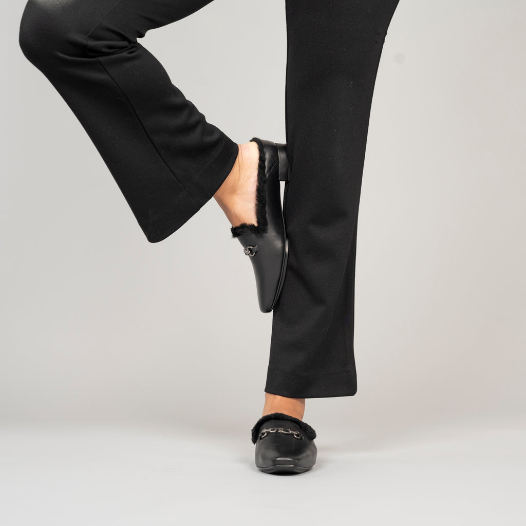 Scarlett Chase Weston Black Leather and Black Shearling Mule with an SC accessory | On foot of a model standing with one leg up on a grey background