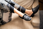 Scarlett Chase Weston Black Leather and Black Shearling Mule with an SC accessory | Person wearing black loafers and patterned pants sitting on a beige couch.