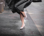 Scarlett Chase taupe embossed leather Amore 55 Pump with a rounded upper and block heel | 3/4 view on feet black skirt on model running on black street in city front foot on ground back leg bent and whole shoe off ground 
