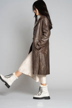 Woman standing in brown leather jacket, white skirt, kicking out left leg wearing Aspen Boot with white leather and black laces.