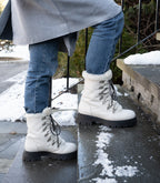 Person standing on snowy stairs outside wearing the Aspen Boot with white leather and black laces.