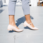 Scarlett Chase Blush Pink Patent Belle Ballet Flat with an adjustable Mary-Jane strap | On foot of a model on their toes while walking on a pier