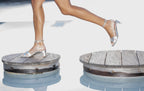 Scarlett Chase champagne metallic nap leather Cali 45 dress sandal with wrap-around ties and a gathered front | Profile on model feet walking in motion with back leg off ground stepping on wooden pods in a pool outside