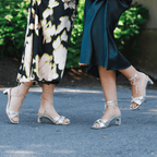 Scarlett Chase silver metallic and champagne napa leather Cali 45 dress sandal with wrap-around ties and a gathered front | 2 models side by side outside on driveway left model has one foot heel raised and profile view other model 3/4 view with back shoe off ground