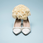 Scarlett Chase Gloria 55 Pump in White Satin with a white satin bow | front view On pair shoes with yellow bouquet on light blue background