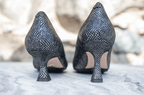 Scarlett Chase black metallic snake leather Grace 55 Pump with a V-cut upper and sculpted heel |  and sculpted heel and black metallic snake Soiree 75 pump with a V-cut upper and sculted heel | detail of back of 1 heel of each style on marble base and marble background