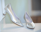 Scarlett Chase silver lame Scarlett Chase Grace 55 Pump with a V-cut upper and sculpted heel | 3/4 view of right show with heel against windowsill left shoe frontal view on counter with muted green colored background
