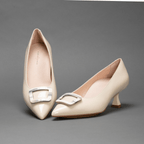 Scarlett Chase nude patent Greta 55 Pump with a rounded upper, sculpted heel, and horn toe accessory | Right shoe top down heel in air left shoe 3/4 view on gray background