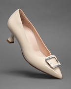 Scarlett Chase nude patent Greta 55 Pump with a rounded upper, sculpted heel, and horn toe accessory | Single shoe on toe heel in air on gray background
