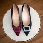 Scarlett Chase bordeaux suede / sangria toe accessory and midnight suede with blue accessory Greta 55 Pump with a rounded upper and sculpted heel  | Single shoes top down on circular white pedestal on wooden flooring