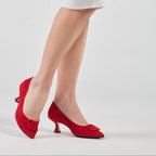 Scarlett Chase Rouge suede Greta 55 Pump with a rounded upper, sculpted heel, and red toe accessory | On feet back shoe has heel off the ground and on toe other shoe is 3/4 view on ground on white background
