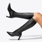 Scarlett Chase knee-high stretch onyx vegan leather Lola 75 boot with a block heel | On model bare legs staggered top leg in air bottom leg heel resting on ground on white background
