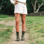 Scarlett Chase ankle stretch moss suede Maya 55 bootie with a block heel  |  On model in outdoor green setting front view 