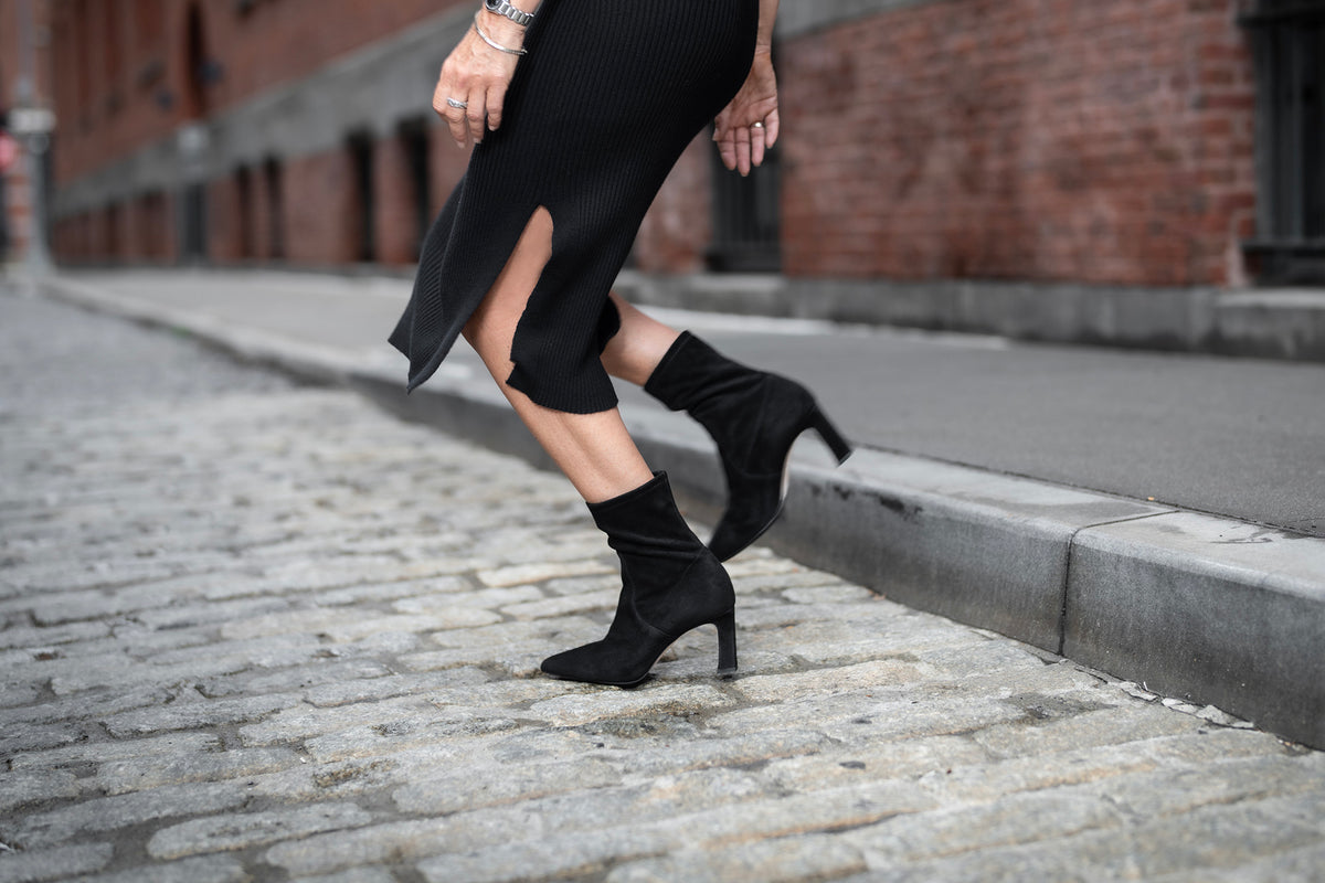 Person wearing black high-heeled boots on a cobblestone street.