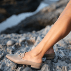 Scarlett Chase Weston Mule in Taupe Napa with an SC gold accessory | Side view on feet with rock background