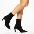Scarlett Chase ankle stretch black suede Portia 75 bootie with a block heel | Side view on model walking with one leg gent and bootie in air on white background